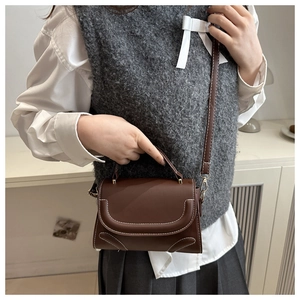 Close-up of brown vintage square bag with white contrast stitching and gold metal buckle