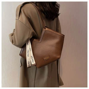 Detail of a brown ribbed tote bag with heart shape and canvas ribbon worn by model