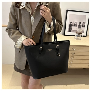Close-up of black leather tote bag with gold logo and adjustable shoulder strap buckle