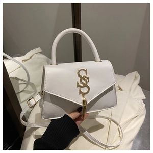 Detail view of white trapezoid handbag with gold S logo and metallic tassel accents