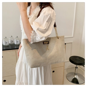 Close-up of beige canvas tote with gold deer charm and leather chain shoulder strap