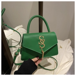 Detail of green leather handbag featuring a gold S-logo with tassel and shoulder strap