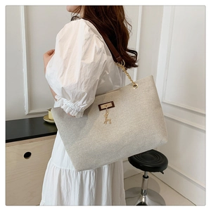 Detail of beige canvas tote bag featuring brown leather strap and golden deer pendant
