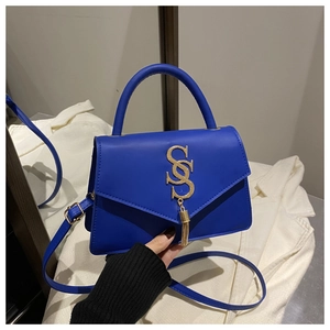 Close-up of royal blue handbag featuring a gold SS logo and elegant metal tassel detail