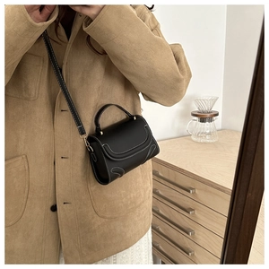 Detail of black leather handbag featuring contrast white stitching and gold hardware