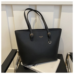 Close-up of black textured leather tote bag with gold logo and side buckle details