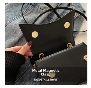 Detailed macro view of the golden metal magnetic clasp on a black matte leather square bag