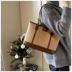 Detail of woven tote bag with brown leather trim and fashion label on creamy base