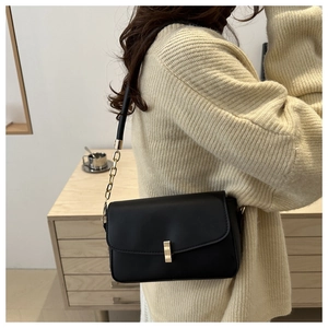 Detail of black matte leather shoulder bag featuring gold buckle and chain strap on model
