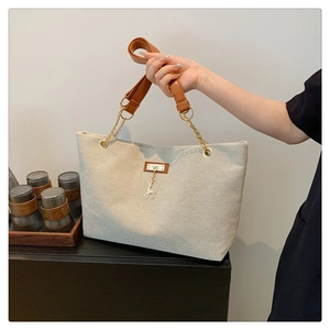 Close-up of beige canvas tote bag with brown leather strap and golden deer pendant