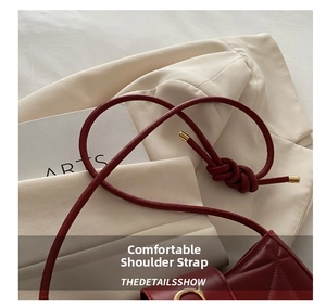 Detail of burgundy leather shoulder bag with knotted strap and gold C-shaped metal hardware