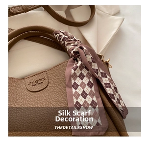 Detail of a brown lychee grain leather handbag featuring a red-brown geometric silk scarf