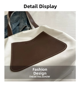 Detailed close-up of white canvas tote bag with brown leather handles and logo engraving
