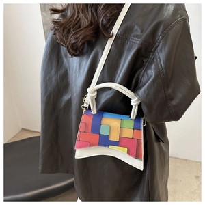 Detail of color-block flap and unique curved base on a white leather crossbody bag