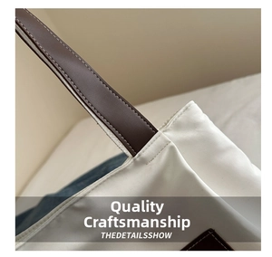 Detail of reinforced double stitching on brown straps of a white nylon tote bag