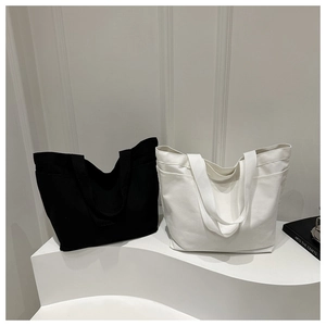 Minimalist canvas tote bag detail showing side pocket and long shoulder straps in black and white