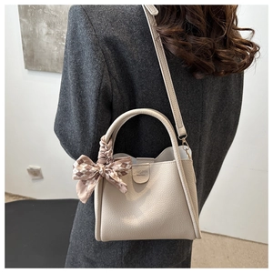 Detail of beige lychee leather bucket bag with decorative silk scarf and metal hardware