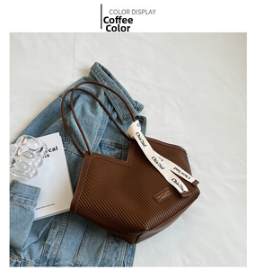 Detail of a brown pleated tote bag with chic ribbon and brand tag on denim background