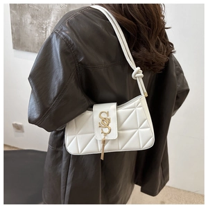 Detail of white quilted underarm bag featuring a gold S-logo and stylish metal tassels