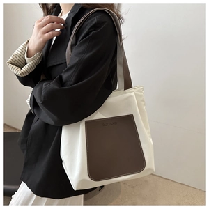 Detail of white canvas tote bag featuring brown leather pocket and long shoulder straps