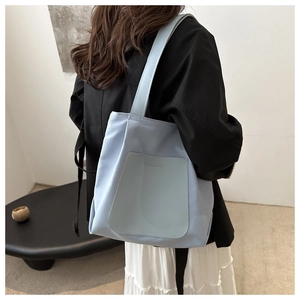 Side view of a light blue nylon tote bag worn by a model in a minimalist room