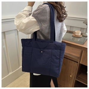 Detail of blue quilted tote bag showing vertical stitching and metal snap closure texture