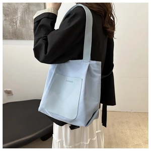 Detail view of light blue nylon tote bag with leather pocket and Budbao logo on shoulder