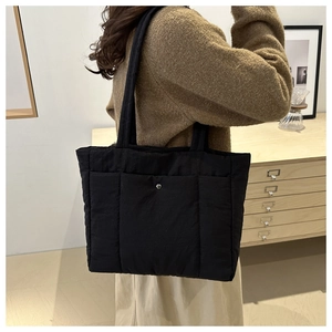 Detail of black quilted tote bag with silver snap button and winter puffer texture