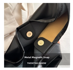 Detail shot of the magnetic snap closure on a black leather tote bag with yellow lining