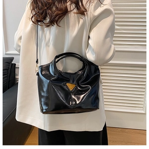 Detailed view of a black glossy handbag with a triangular logo on a white blazer