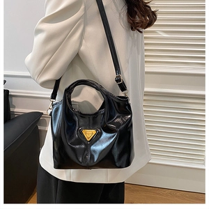 Detail of black patent leather handbag with gold metal logo and sleek adjustable strap