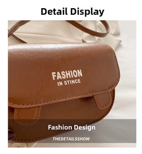 Detail of brown textured leather saddle bag with white lettering and flap closure