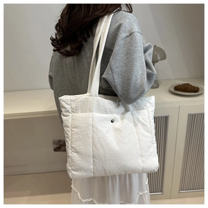 Detail of white quilted tote bag with metal snap pocket on model in minimalist interior