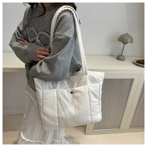 Side view of white quilted puffer tote bag on shoulder, showcasing its large capacity size