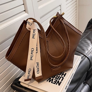 Deep brown pleated tote bag with vertical texture and stylish logo strap on books