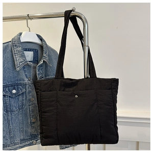 Detail of a black quilted tote bag with a silver metallic snap button and soft texture