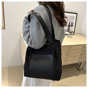 Detailed side view of a large black nylon tote bag with a leather pocket and shoulder strap