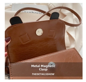 Detail view of the metal magnetic buckle closure on a brown vintage textured saddle bag