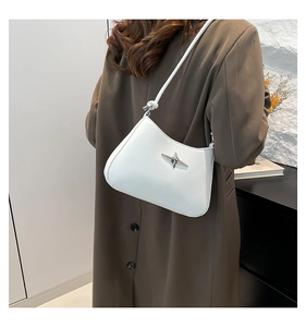 Primer plano de bolso bandolera blanco minimalista con estrella plateada y gabardina marrón