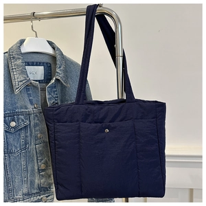 Detail of dark blue quilted tote bag with vertical stitching and metal snap pocket