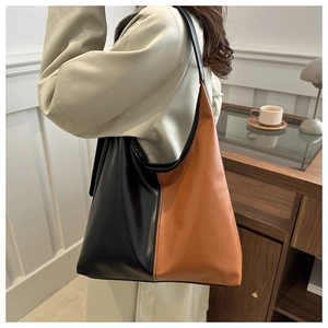 Fashionable minimalist tote bag in black and tan contrast worn with light winter coat