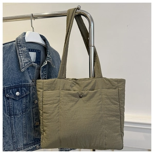 Detail of olive green quilted tote bag with front snap pocket on a minimalist display