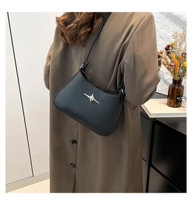 Detalle de bolso de hombro en cuero negro con estrella de plata sobre abrigo de lana