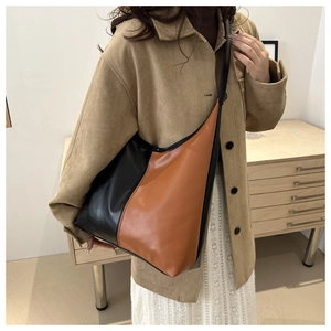 Detail of a large two-tone leather hobo shoulder bag worn by a model in a warm room