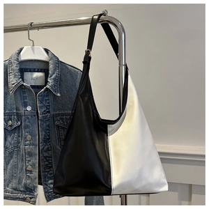 Detail of minimalist black and white bicolor faux leather tote bag hanging on metal rack