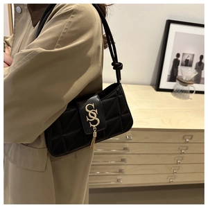 Quilted black underarm bag with gold S logo and tassel detail worn by a model in interior
