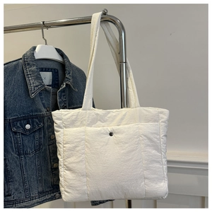 Detail of white quilted nylon tote bag featuring front snap pocket and soft padded texture