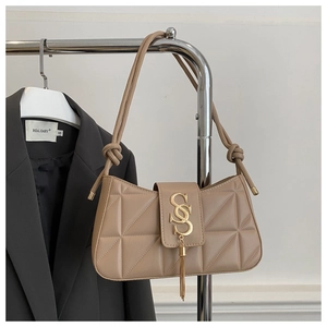 Close-up of beige quilted baguette bag with gold S-buckle and metal chain tassels