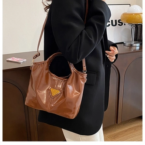 Detail of glossy brown leather bucket bag with gold triangle hardware on female model
