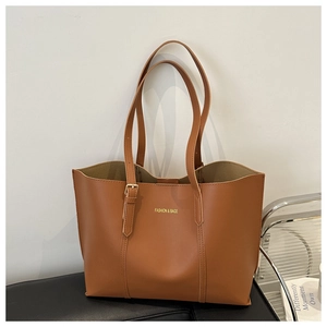Détail d'un grand sac cabas en cuir marron avec lettrage doré sur une surface noire
